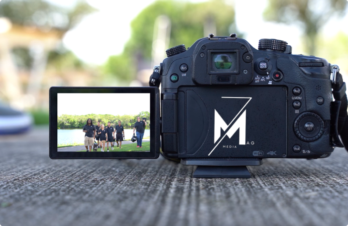A camera perched on a concrete surface captures a vivid video of people walking outdoors, with a company logo proudly displayed on its body.